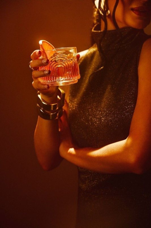 A guest in amber light, holding a rose-colored cocktail